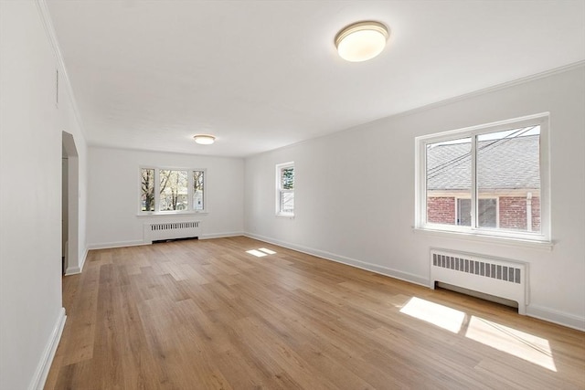 unfurnished living room with light wood-type flooring, arched walkways, radiator, and baseboards