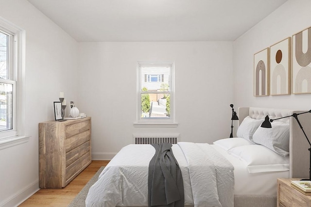 bedroom with baseboards, light wood-style flooring, radiator, and multiple windows