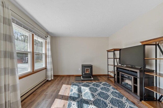 sitting room with a baseboard radiator, wood finished floors, baseboards, and a wood stove