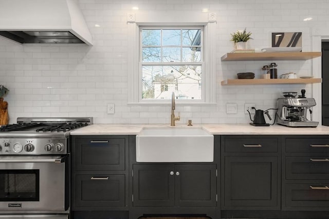 kitchen featuring a sink, backsplash, light stone countertops, custom exhaust hood, and stainless steel gas range