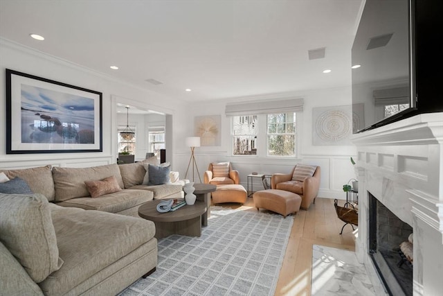 living room with a high end fireplace, light wood finished floors, visible vents, ornamental molding, and a decorative wall