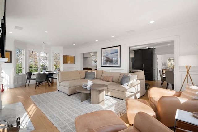 living room featuring recessed lighting, light wood finished floors, crown molding, and a decorative wall