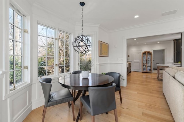 dining area featuring a decorative wall, wainscoting, light wood-type flooring, and ornamental molding