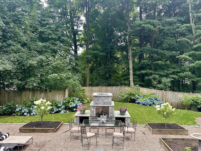 view of patio / terrace with a grill, an outdoor stone fireplace, a fenced backyard, and a garden