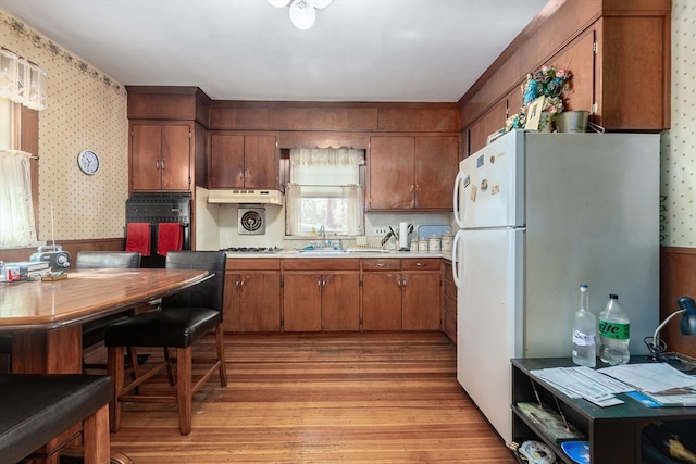 kitchen with light hardwood / wood-style floors, white fridge, sink, and black oven