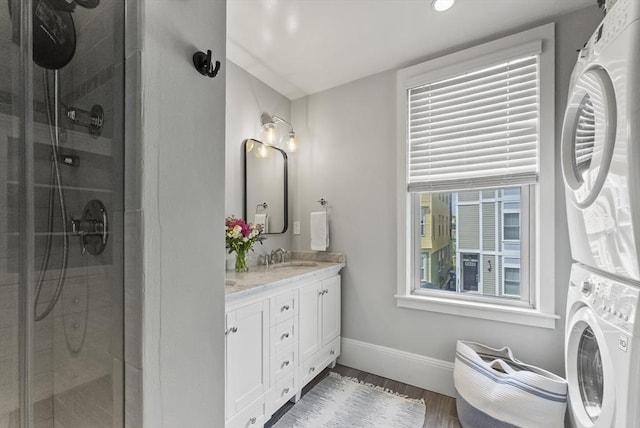 bathroom with stacked washer / drying machine, baseboards, a shower stall, vanity, and wood finished floors
