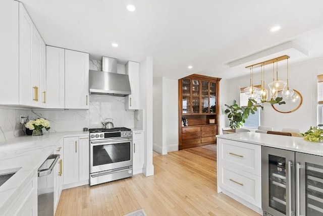 kitchen with appliances with stainless steel finishes, wall chimney range hood, wine cooler, backsplash, and white cabinetry
