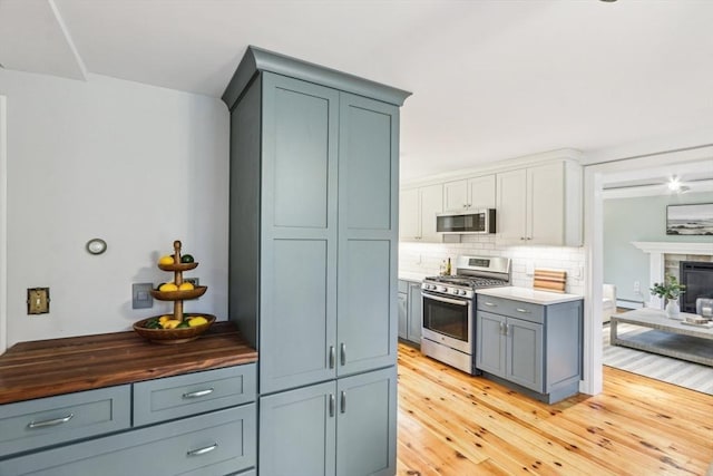 kitchen with light wood-type flooring, stainless steel appliances, tasteful backsplash, and a glass covered fireplace