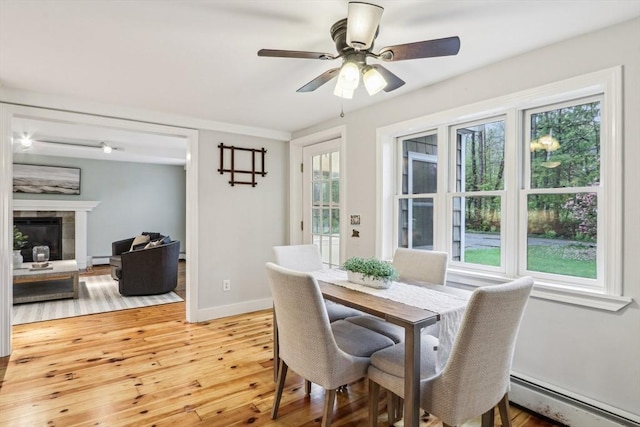 dining space featuring a ceiling fan, a baseboard radiator, light wood finished floors, and plenty of natural light