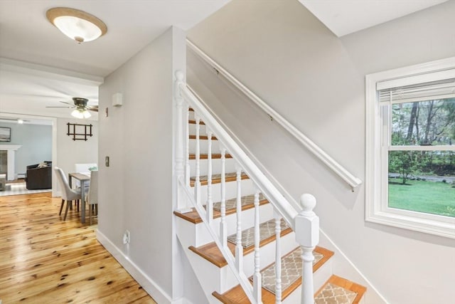 stairway featuring a ceiling fan, baseboards, a fireplace, and wood-type flooring