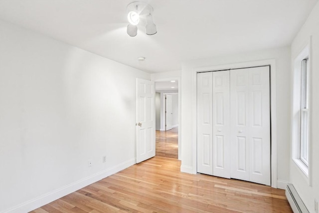 unfurnished bedroom featuring light wood finished floors, a closet, baseboards, and a baseboard heating unit