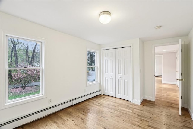 unfurnished bedroom featuring light wood-style flooring, a closet, baseboards, a baseboard heating unit, and a baseboard radiator