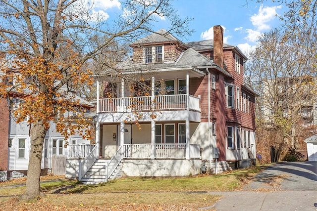 view of front facade featuring a porch, roof with shingles, a front yard, a chimney, and a balcony