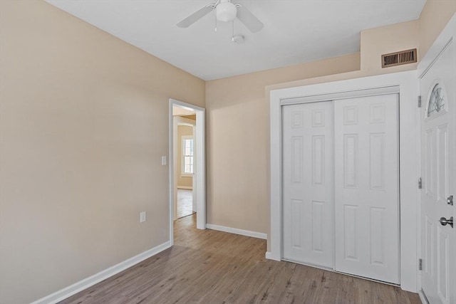 unfurnished bedroom featuring wood finished floors, visible vents, baseboards, ceiling fan, and a closet