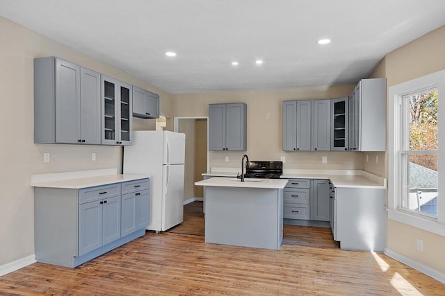 kitchen featuring a kitchen island with sink, a wealth of natural light, gray cabinets, and freestanding refrigerator