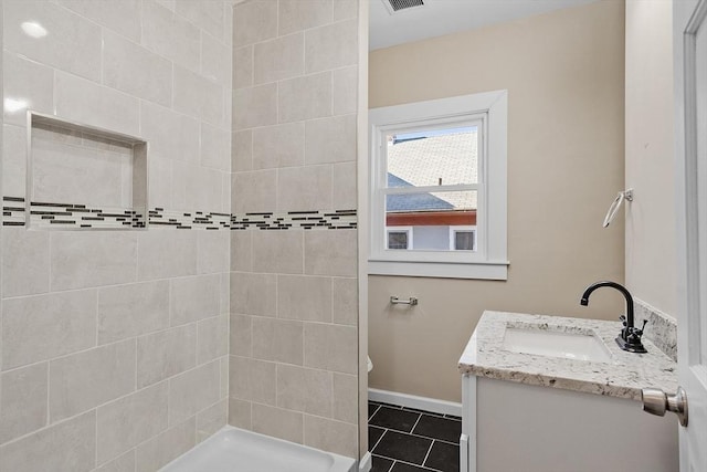 bathroom featuring visible vents, baseboards, tiled shower, tile patterned floors, and vanity