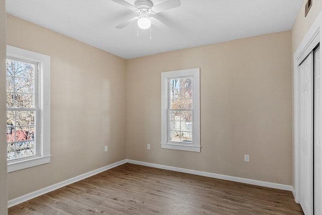 unfurnished bedroom with a closet, multiple windows, baseboards, and wood finished floors