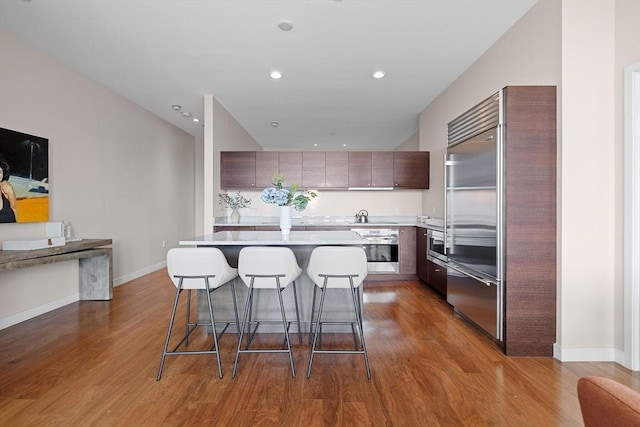 kitchen featuring stainless steel appliances, a breakfast bar, light countertops, dark wood-style floors, and recessed lighting