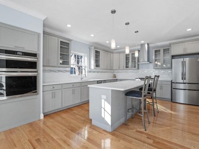 kitchen with decorative light fixtures, wall chimney range hood, a center island, appliances with stainless steel finishes, and gray cabinetry