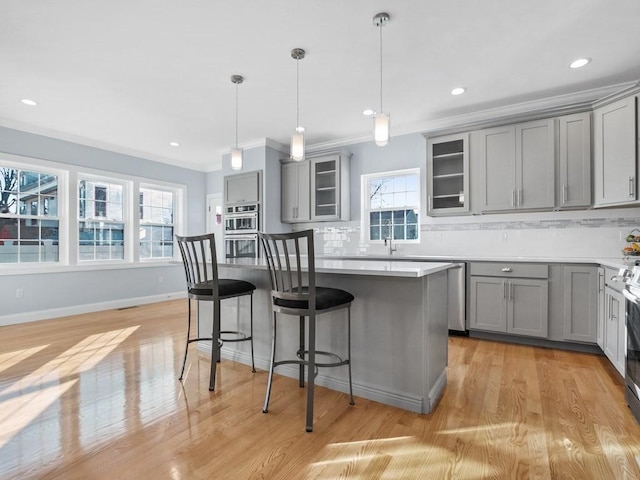 kitchen featuring a kitchen island, decorative light fixtures, backsplash, a breakfast bar, and gray cabinetry