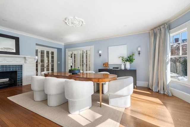 dining space featuring a fireplace, baseboards, french doors, light wood finished floors, and crown molding