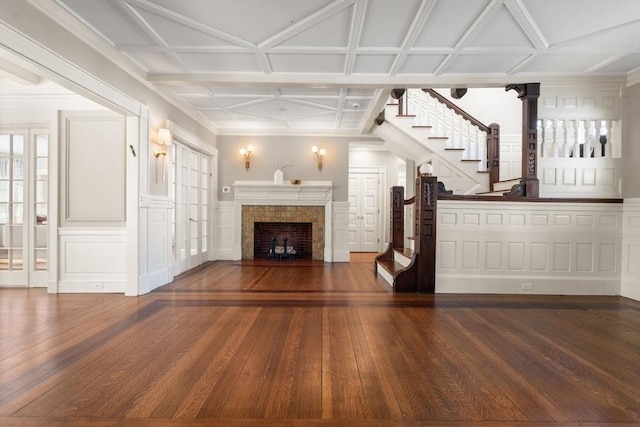 unfurnished living room featuring wood-type flooring, stairs, coffered ceiling, and a tile fireplace