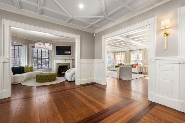 unfurnished living room with coffered ceiling, wood finished floors, crown molding, a fireplace, and a notable chandelier