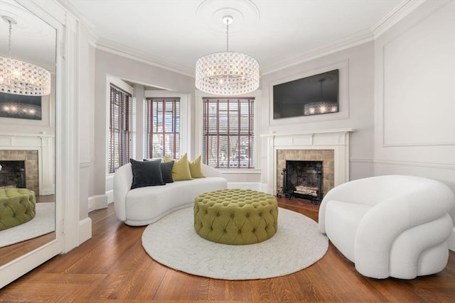 sitting room featuring a chandelier, wood finished floors, a tile fireplace, and ornamental molding