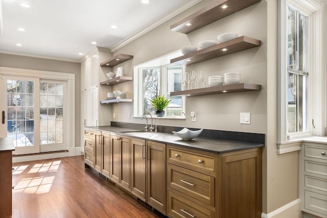 kitchen featuring a sink, a healthy amount of sunlight, open shelves, brown cabinetry, and dark countertops