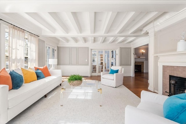 living area featuring a healthy amount of sunlight, a fireplace, beamed ceiling, and wood finished floors