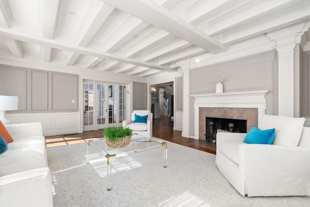 living area with beamed ceiling, a tiled fireplace, wood finished floors, and a decorative wall