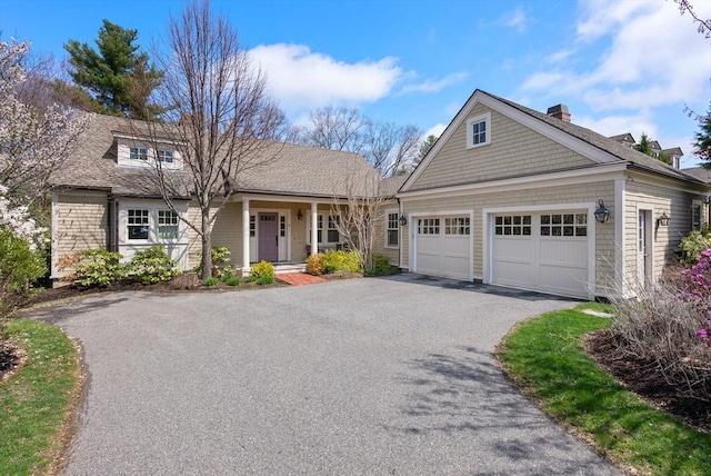 view of front of home featuring a chimney, aphalt driveway, a shingled roof, an attached garage, and a porch