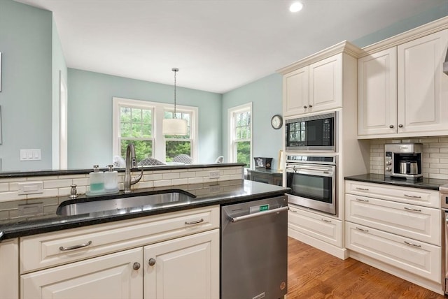 kitchen with stainless steel appliances, a sink, dark stone countertops, light wood-style floors, and backsplash