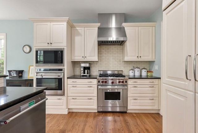 kitchen with dark countertops, tasteful backsplash, wall chimney exhaust hood, and appliances with stainless steel finishes