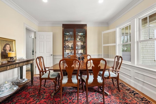 dining space featuring a wainscoted wall, wood finished floors, ornamental molding, and a decorative wall