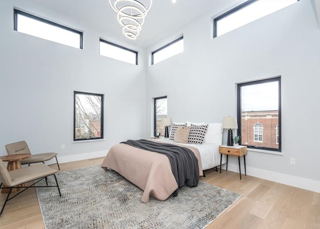 bedroom featuring light wood-type flooring, baseboards, a towering ceiling, and an inviting chandelier