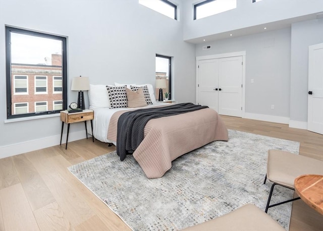 bedroom featuring visible vents, wood finished floors, baseboards, a closet, and a high ceiling