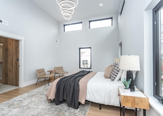 bedroom featuring a high ceiling, a chandelier, baseboards, wood finished floors, and visible vents