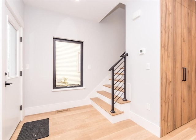 foyer entrance with baseboards, visible vents, light wood finished floors, and stairs