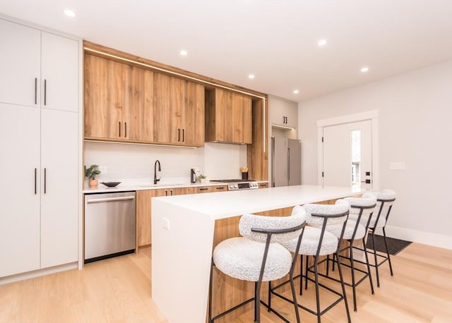 kitchen with a sink, appliances with stainless steel finishes, light wood-type flooring, and light countertops