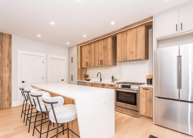 kitchen with a kitchen island, light wood-style floors, light countertops, a sink, and appliances with stainless steel finishes