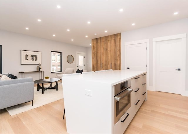 kitchen with a kitchen island, open floor plan, stainless steel oven, light countertops, and light wood finished floors