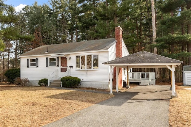 view of front facade featuring a chimney, a detached carport, and driveway