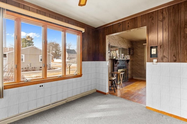 unfurnished room featuring a brick fireplace, wood walls, a wealth of natural light, and carpet floors