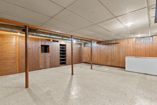 finished below grade area featuring tile patterned floors, wooden walls, fridge, and a paneled ceiling