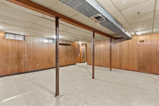 basement with tile patterned floors, a drop ceiling, wooden walls, and stairs