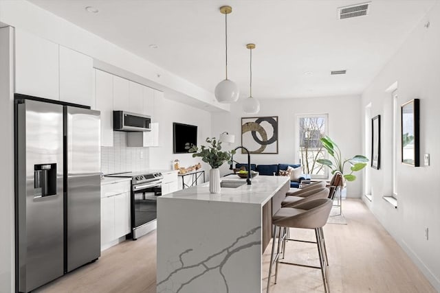 kitchen with pendant lighting, a center island with sink, white cabinets, decorative backsplash, and stainless steel appliances