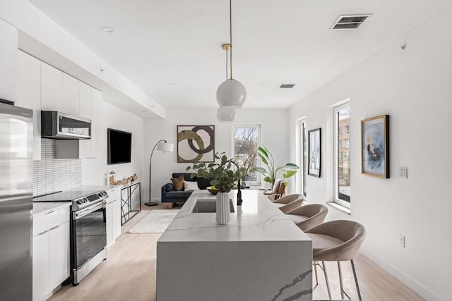 kitchen with a kitchen bar, stainless steel appliances, decorative light fixtures, white cabinets, and a center island