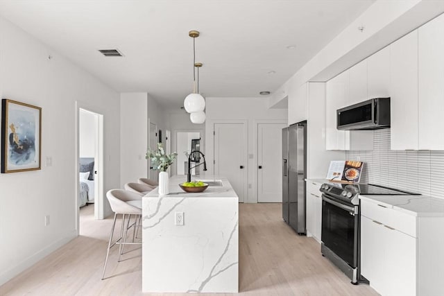 kitchen with sink, an island with sink, pendant lighting, white cabinets, and appliances with stainless steel finishes