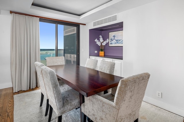 dining area with light hardwood / wood-style flooring, a tray ceiling, and a water view